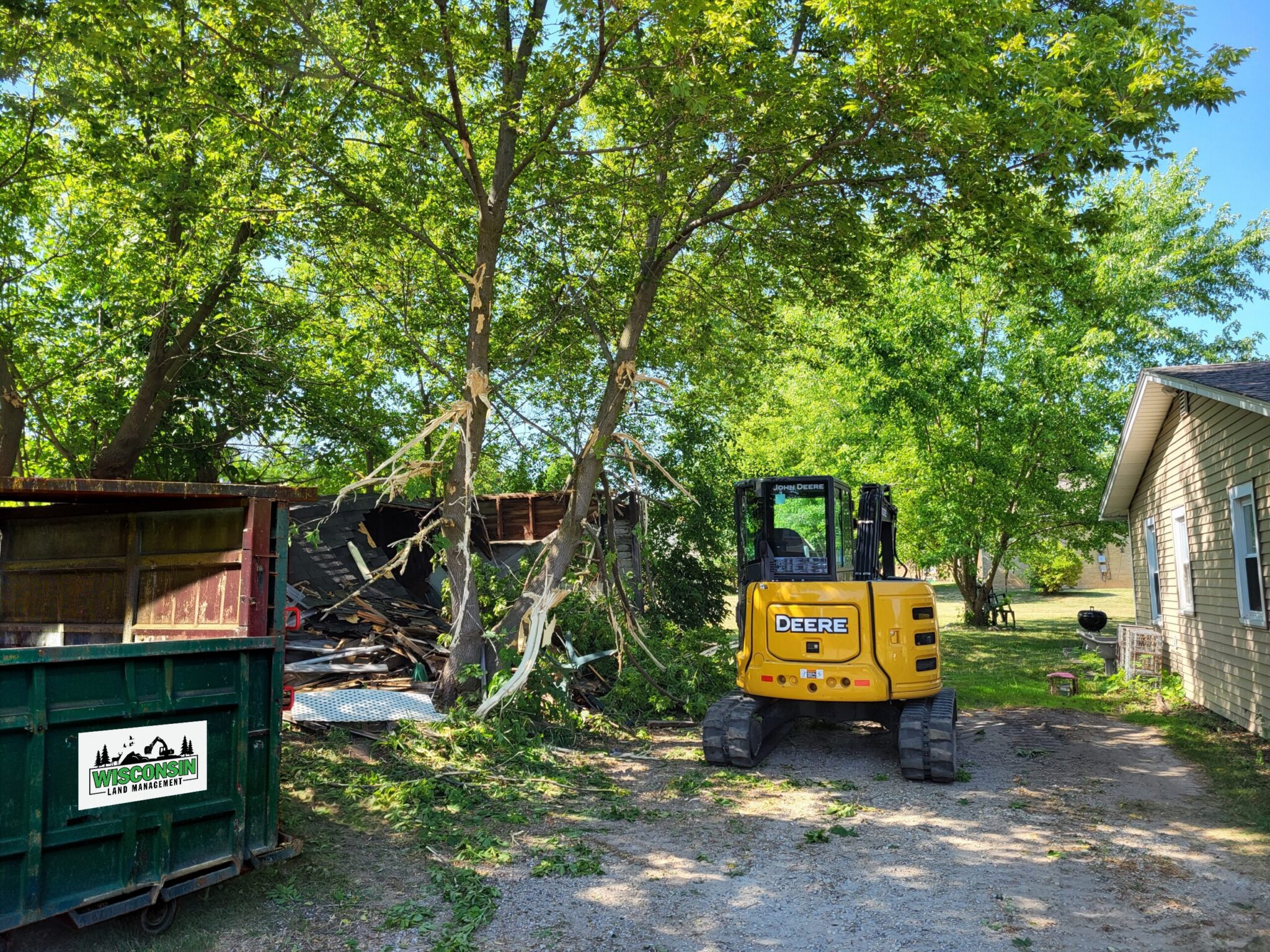 Demolition Services A John Deere excavator and a branded WLM dumpster clearing debris from a building demolition site in Wisconsin.