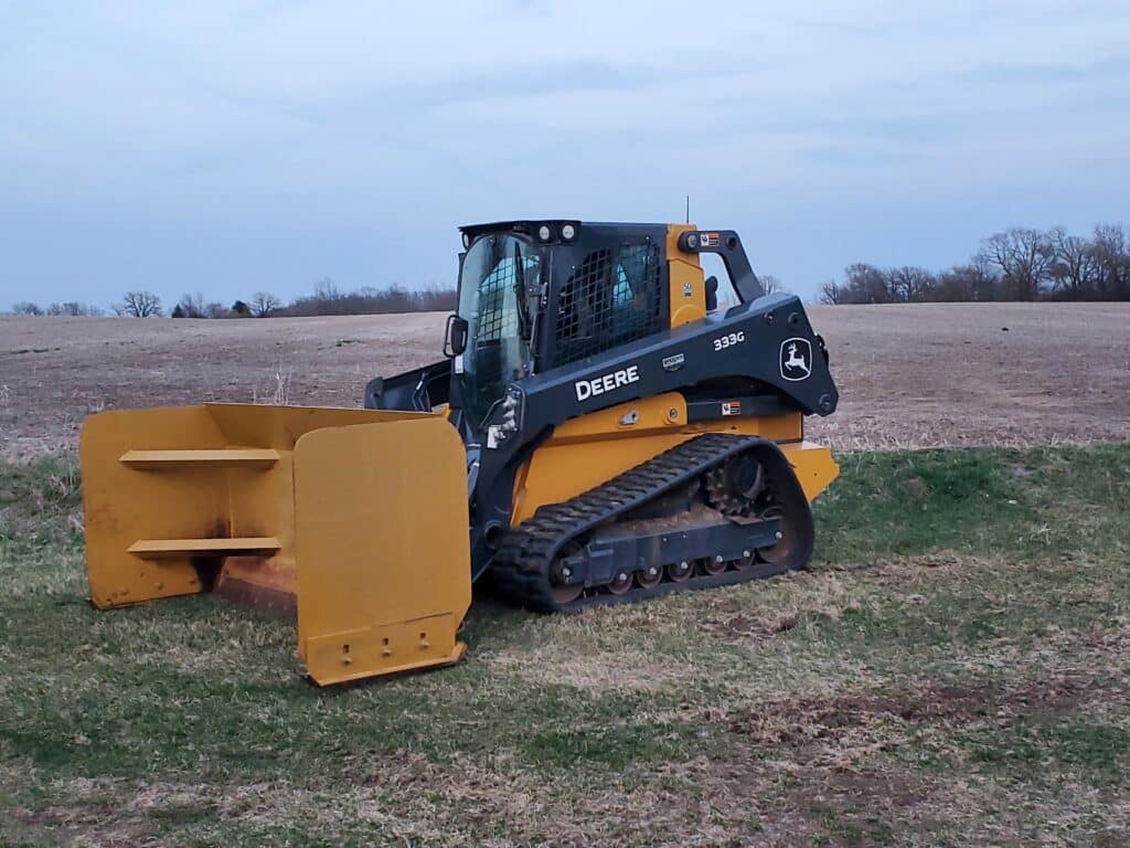 A John Deere 333G compact track loader equipped with a large grading blade, parked on a job site in Wisconsin.