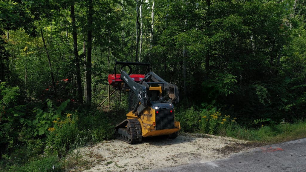 A John Deere compact track loader with a forestry mulcher clearing brush along a power line right-of-way in Wisconsin.