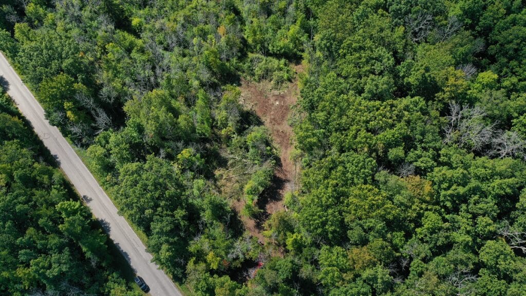 An aerial view of a building site cleared in a dense forest, showing the transformation of raw land into a build-ready property.
